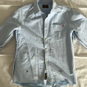 Ljusblå skjorta från Replay - Säljer en ljusblå skjorta från Replay med en bröstficka och broderad logga. Skjortan har långa ärmar och knappar framtill. Perfekt för en avslappnad stil.