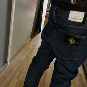 Mörkblå jeansbyxor från Stone Island - Snygga mörkblå jeansbyxor från Stone Island med en unik design. Byxorna har en normal passform och är dekorerade med det ikoniska Stone Island-märket på bakfickan. Perfekta för en stilren look.för fler bilder kom privat!