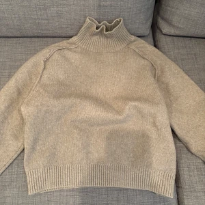 Beige stickad polotröja - Säljer en mysig beige stickad polotröja med ribbade detaljer vid krage, ärmslut och nederkant. Perfekt för kyliga dagar och ger en stilren look. Passar bra till både jeans och kjol.