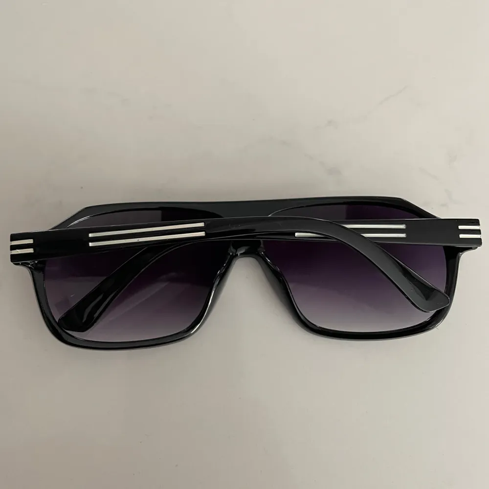 Snygga svarta solglasögon med en klassisk design och silverdetaljer på bågarna. De har mörka linser som ger ett coolt intryck och skyddar mot solen. Perfekta för en stilren look.. Asusteet.