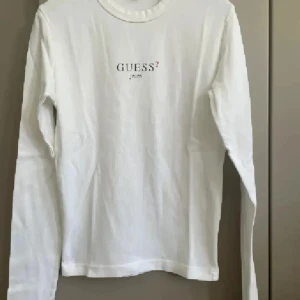 Vit långärmad tröja från Guess - Säljer en stilren vit långärmad tröja från Guess med logotypen tryckt på bröstet. Perfekt för en avslappnad look. Tröjan är gjord i ett mjukt material som känns skönt mot huden.