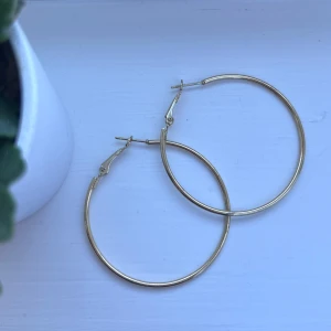 Guldiga hoops - Snygga och stilrena guldiga hoop-örhängen. Perfekta för att ge en elegant touch till din outfit. De har en enkel låsmekanism som gör dem lätta att ta på och av. Önskar du veta exakta mått? Tveka inte att höra av dig!