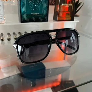 Solglasögon - Snygga svarta solglasögon med en cool design och metallbågar. De har en klassisk aviator-stil med mörka linser som ger ett stilrent intryck. Perfekta för soliga dagar och en stilfull look.