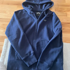 Mörkblå hoodie från Hollister - Säljer en mörkblå hoodie från Hollister Must-Have Collection. Den har en dragkedja framtill och en klassisk huva. Perfekt för en avslappnad stil. 🌀
