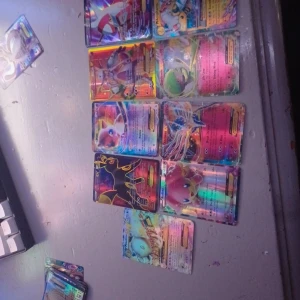 Pokémon-kort 9 st - Samling av Pokémon-kort med färgglad holografisk design. Perfekt för samlare eller spelentusiaster. Kortens baksida har den klassiska blå designen med en Pokéball i mitten.