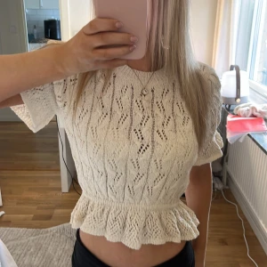 Vit stickad topp med volangdetalj - Säljer en söt vit stickad topp med korta ärmar och volangdetalj där nere och i armarna. Toppen har ett fint hålmönster och en rund halsringning. Använd några gånger men den har inga defekter.