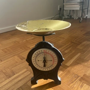 Retro köksvåg med guldfärgad skål - Charmig retro köksvåg med en rund guldfärgad skål. Vågen har en klassisk design med en svart bas och en tydlig mätare i mitten. Perfekt för att ge köket en vintage känsla eller för att användas vid bakning och matlagning.