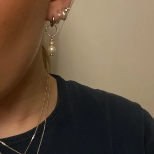 Silverörhängen med pärlor - Snygga silverörhängen med en vriden design och hängande pärlor. Perfekta för att ge en elegant touch till din stil. I äkta silver förutom själva ”hoopsen” som är i rostfritt stål. Den översta pärlan är äkta sötvattens pärla. 