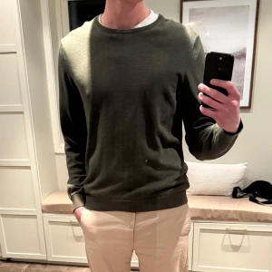 Olivgrön tröja - Säljer en stilren olivgrön tröja med rund halsringning. Tröjan har långa ärmar och ribbade muddar vid ärmslut och nederkant. Perfekt för en avslappnad look.