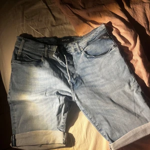 Blå jeansshorts från Replay - Snygga äkta blå jeansshorts från Replay med klassisk femficksdesign och uppvikta benslut. Perfekta för en avslappnad stil. Märkesdetaljer på baksidan ger en extra touch.