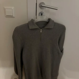 Grå ribbad tröja från Zara - Säljer en stilren grå ribbad tröja från Zara med dragkedja framtill. Tröjan har långa ärmar och en hög krage som ger en snygg look. Perfekt för kyligare dagar!