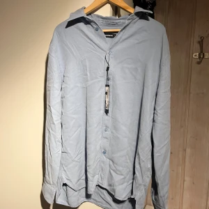 Ljusblå skjorta från J.Lindeberg - Snygg ljusblå skjorta från J.Lindeberg med klassisk krage och knappar framtill. Perfekt för en stilren look. Skjortan har långa ärmar och är tillverkad i ett mjukt material.