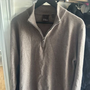 Beige/ljusbrun halfzip från Oscar Jacobson - Säljer en stilren tröja från Oscar Jacobson med dragkedja i halsen. Tröjan är långärmad och tillverkad i ett mjukt material, perfekt för kyligare dagar. Den har en klassisk design som passar till många tillfällen.