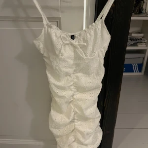 Vit klänning med spetsdetaljer - Säljer en söt vit klänning med spetsdetaljer och rynkade detaljer.  Klänningen har en åtsittande passform och  är i storlek XS. Bara använd en gång på en skolavslutning 🤍