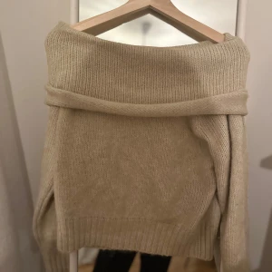 Beige stickad offshoulder tröja - Säljer en mysig beige stickad tröja med offshoulder-design. Perfekt för kyliga dagar med sin mjuka och bekväma passform. Tröjan har långa ärmar och ribbade kanter som ger en stilren look. Passar utmärkt till både jeans och kjol.