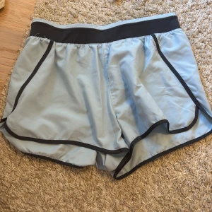Ljusblå träningsshorts med mörk blå detaljer - Snygga ljusblå träningsshorts med mörk blå kanter och elastisk midja. Perfekta för en aktiv livsstil och bekväma att bära under träning. De har en sportig look med en lös passform.