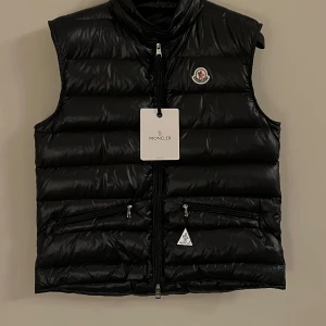 Svart dunväst från Moncler - Snygg svart dunväst från Moncler med dragkedja och logotyp på bröstet. Perfekt för kyliga dagar