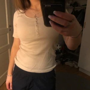 Beige ribbad topp från H&M - Säljer en stilren beige ribbad topp från H&M med korta ärmar och knappar framtill. Perfekt för en avslappnad look. 🧡