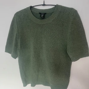 Grön stickad tröja från Lindex - Säljer en stilren grön stickad tröja från Lindex. Tröjan har korta ärmar och en rund halsringning, perfekt för en avslappnad look. Storlek XS.
