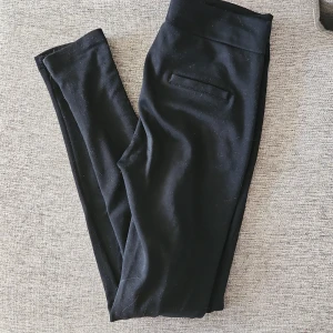 Svarta byxor med dragkedja - Snygga svarta leggings byxor med fejkade dragkedjor framtill. De har en smal passform och är perfekta för en stilren look. Byxorna har en elastisk midja för extra komfort.
