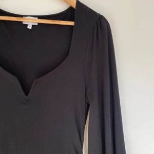 Svart långklänning med v-ringning - Elegant svart långklänning med v-ringad hals och långa ärmar. Klänningen har en smickrande passform och är perfekt för en stilren look. Materialet är mjukt och följsamt, vilket gör den bekväm att bära. Scrunch i midjan för mer smickrande passform och lätt ballongformade ärmar. 