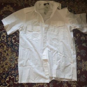 Vit kortärmad skjorta med fickor - Säljer en klassisk vit kortärmad skjorta med två bröstfickor och knappar framtill. Perfekt för en stilren och avslappnad look. Skjortan har en normal passform och är tillverkad i ett lätt och bekvämt material. Köpt på Björk i Malmö för 150 kr prislapp finns kvar, bara provad ej använd