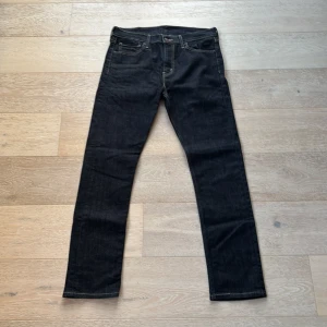 Levis jeans i mörkblå denim - Snygga Levis jeans i mörkblå denim med klassisk femficksdesign och knappgylf. De har en slim passform som ger en modern look. Perfekta för dig som vill ha stilrena och tidlösa jeans.