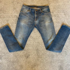 Blå jeans från Nudie Jeans - Snygga blå jeans från Nudie Jeans med klassisk femficksdesign och orange sömmar. Storleken är 30/32