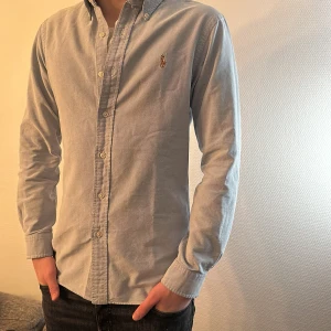 Blå skjorta från Ralph Lauren - Snygg blå skjorta från Polo Ralph Lauren i S. Skjortan har långa ärmar och en broderad logotyp på bröstet. Perfekt för en stilren look.