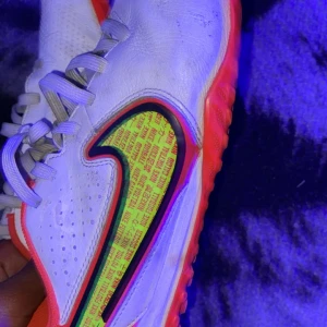 Vita fotbollsskor från Nike - Snygga vita fotbollsskor från Nike med neonfärgade detaljer och snörning. Skorna har en iögonfallande design med en färgglad sula och insida. Perfekta för fotbollsplanen med sin stilrena look och funktionella passform.