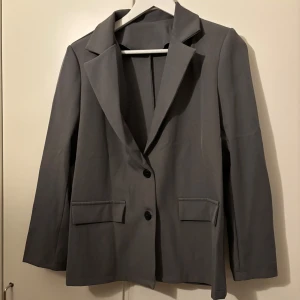 Grå kavaj - Snygg grå kavaj med klassisk design och två knappar framtill. Perfekt för en stilren look. Passar bra till både jeans och kostymbyxor.