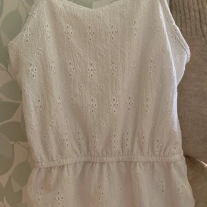 Vitt linne från Kappahl - Söt vit blus från Kappahl med broderade detaljer. Blusen är ärmlös och har en elastisk midja för en bekväm passform. Perfekt för varma sommardagar! 🌼               Den är i strl 134-140 men jag skulle säga att den är som en 152!💕