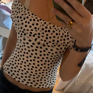 Prickig offshoulder topp - Säljer en söt offshoulder topp med svart prickigt mönster på vit bakgrund. Toppen har volangdetaljer vid axlarna och är perfekt för en somrig look. Passar bra till både jeans och kjol.
