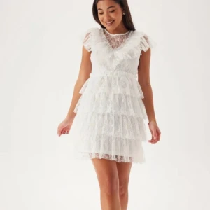 Vit spetsklänning med volanger - Charmig vit spetsklänning med volanger och kort ärm. Klänningen har en v-ringad design och knappar i ryggen. Perfekt inför student eller sommaravslutning ☀️⛱️ köpt för 999kr! lånade bilder  