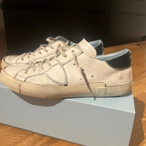 Philippe Model Skor - Snygga vita sneakers från Philippe Model med svarta detaljer och snörning. Perfekta för en avslappnad stil. Skorna kommer i originalkartong. Lite slitna men nästan allt går och laga med lite sko lim. Sulan i skon är ganska sliten fram vid tårna så jag skickar med ett par extra sulor. Och pris går att diskuteras 