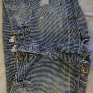 Randiga jeansshorts från Mango - Säljer ett par coola randiga jeansshorts från Mango.👖 De är blå med slitna detaljer och fransar vid benen. Perfekta för en avslappnad stil. Shortsen har en knapp och dragkedja framtill.💞