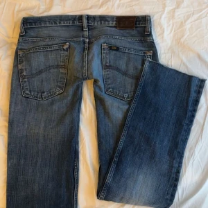 Blå jeans från Lee - Snygga blå jeans från Lee med klassisk femficksdesign och knappgylf. De har en rak passform och är perfekta för en avslappnad stil. Märkeslogga på bakfickan. Innerbensläng:82, midjemått tvärs över:40