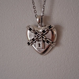 Hjärta med kedja och lås hängsmycke - Unikt hängsmycke i form av ett hjärta med korslagda kedjor och ett låsdetalj. Tillverkat i silverfärgat material, perfekt för att ge en edgy touch till din stil.