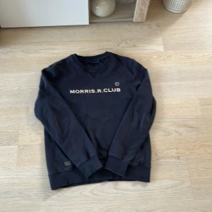 Svart tröja från Morris R. Club - Säljer en stilren svart tröja från Morris R. Club med tryck på bröstet. Tröjan har långa ärmar och en rund halsringning. Perfekt för en avslappnad look.