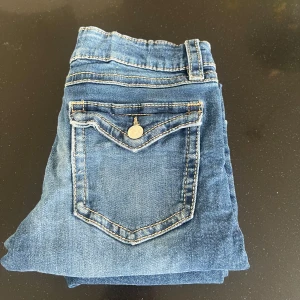 Blå jeansbyxor med bootcut - Snygga blå jeans med bootcut-stil och klassisk femficksdesign. Byxorna har en knapp och dragkedja framtill samt dekorativa sömmar på bakfickorna. Perfekta för en avslappnad look. 