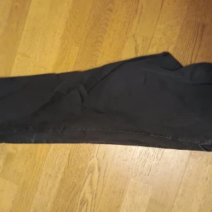 Svarta Chinos - Säljer ett par svarta kostymbyxor i Regular Fit. Byxorna har klassisk rak passform och är perfekta för en stilren look. De är tillverkade i ett mjukt material och har diskreta sömmar längs benen.