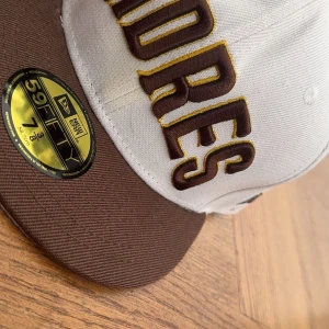 San Diego Padres keps från New Era 59FIFTY - Snygg 59FIFTY keps från New Era med San Diego Padres brodyr framtill. Kepsen är beige med brunt brätte och har klassisk passform. Perfekt för dig som gillar baseball eller streetwear.