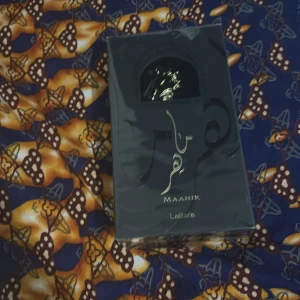 Lattafa Maahir Eau de Parfum 100ml - En elegant parfym från Lattafa, Maahir, i en svart och guldig förpackning. Flaskan rymmer 100 ml Eau de Parfum och har en lyxig design med arabiska detaljer. Perfekt för dig som gillar exklusiva och orientaliska dofter.