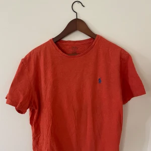 Röd t-shirt från Polo Ralph Lauren - Säljer en röd t-shirt från Polo Ralph Lauren med klassisk passform och rund halsringning. T-shirten har en liten blå broderad logga på bröstet och är tillverkad i mjuk bomull. Perfekt för en avslappnad stil. Skick 9/10 inga tecken på användning.