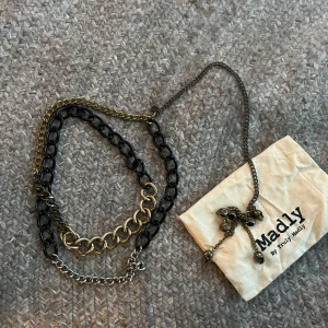 Kedjehalsband från Madly - Säljer ett coolt halsband från Madly med flera kedjor i olika färger: svart, guld och silver. Halsbandet har detaljer med små dödskallar och en mix av grova och tunnare länkar. Perfekt statement-piece för att lyfta din outfit.