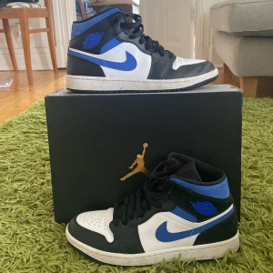 Nike Air Jordan 1 Mid White/Racer Blue-Black - Säljer ett par Nike Air Jordan 1 i fint skick. Dom är synligt använda men det är mest smuts som enkelt går att tvätta bort. Storlek 43 men passar mycket bra även om du har storlek 42. Skriv om ni har frågor! 