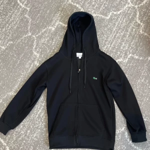 Svart Lacoste zip - Säljer en svart zip hoodie från Lacoste. 55cm längd från krage till bott, 45cm axelbredd.