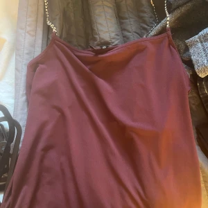 Vinröd linne-topp med pärlband från Vero Moda - Säljer en vinröd linne-topp från Vero Moda med smala axelband dekorerade med pärlor. Toppens material är mjukt och har en elegant känsla, perfekt för att lyfta en outfit.