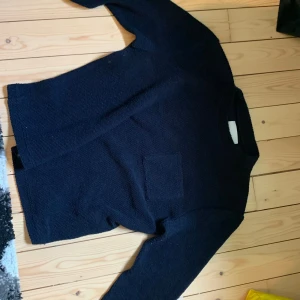 Mörkblå stickad tröja med ficka - Säljer en enkel och stilren mörkblå stickad tröja med rund hals och en liten ficka på bröstet. Tröjan har långa ärmar och passar perfekt till vardags. Klassisk modell som är lätt att matcha.