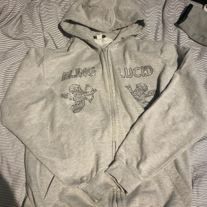 Grå hoodie från Bling Lucid - Grå zip-hoodie från blinglucid.använd kanske två gånger några pärlor är borta men de syns inte så mycket.hör av er vid frågor och pris.